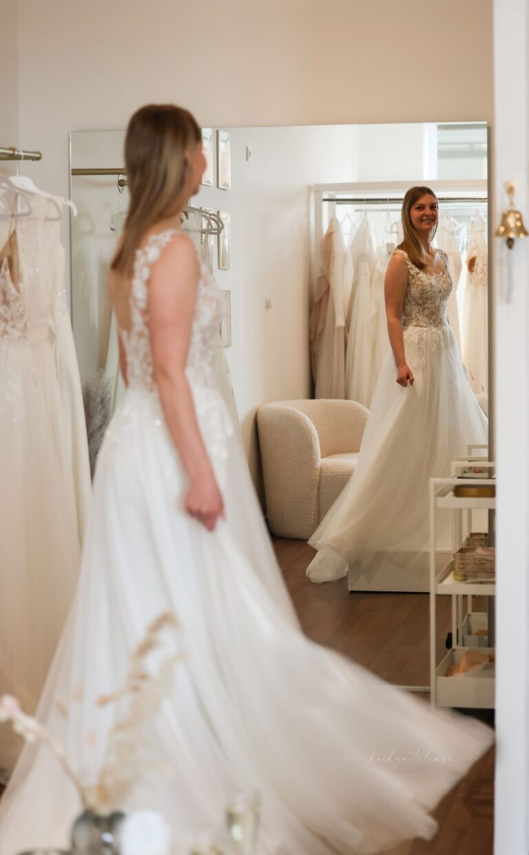 Braut betrachtet ihr Brautkleid im großen Spiegel der Boutique