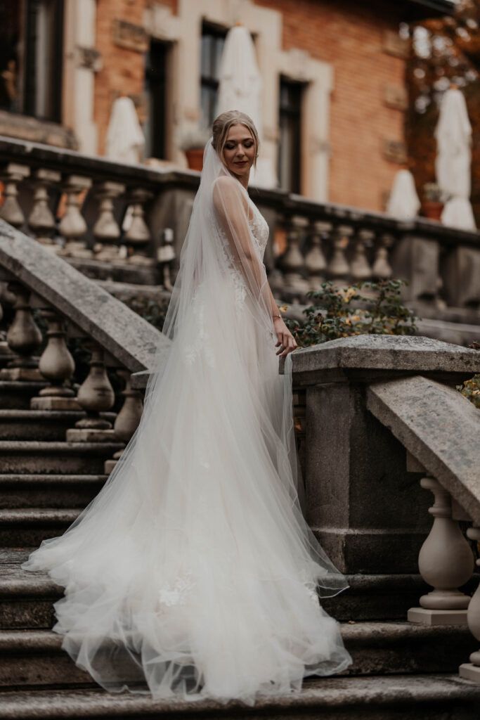 Braut auf einer Schlosstreppe im Tüll Brautkleid mit Schleppe