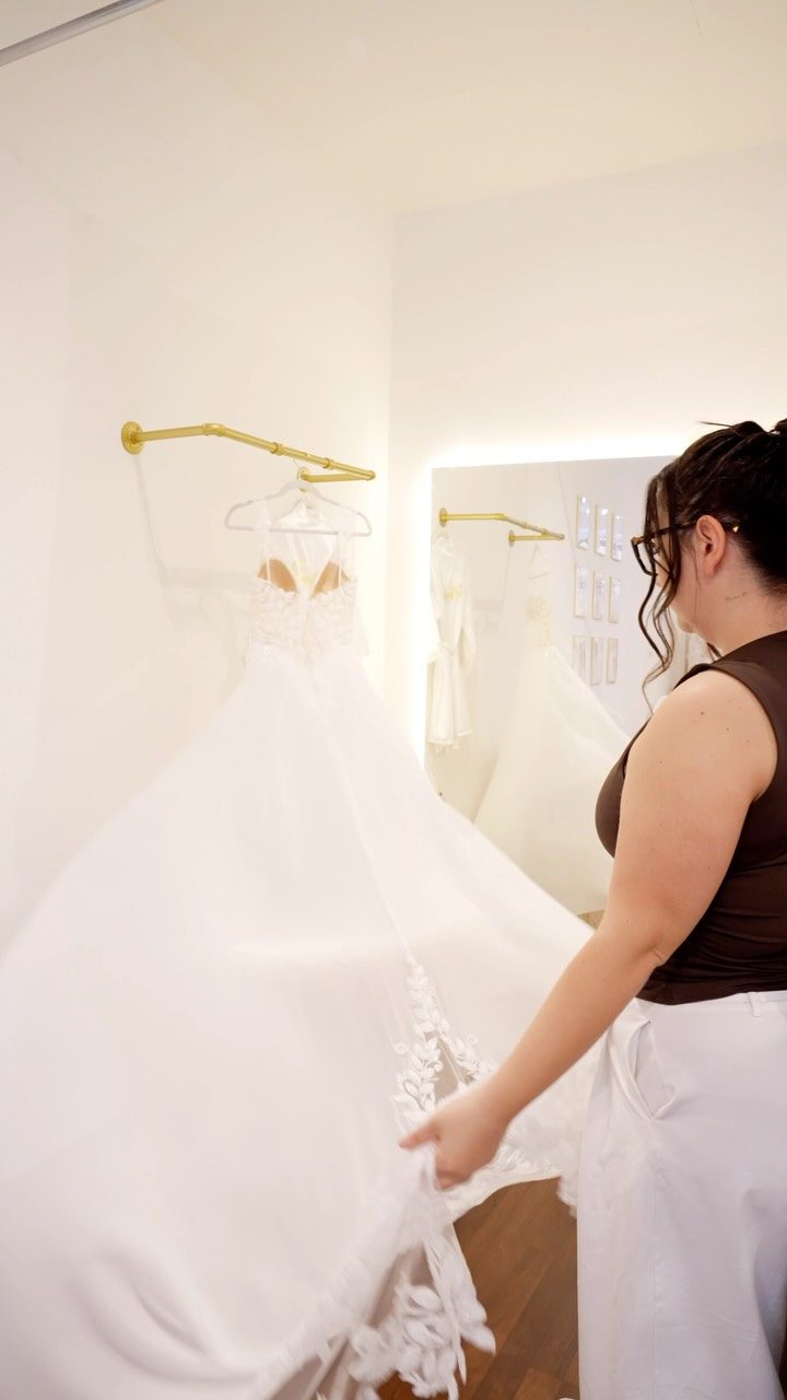 Reel: Beraterin richtet ein Brautkleid mit Spitzenschleppe in der Boutique